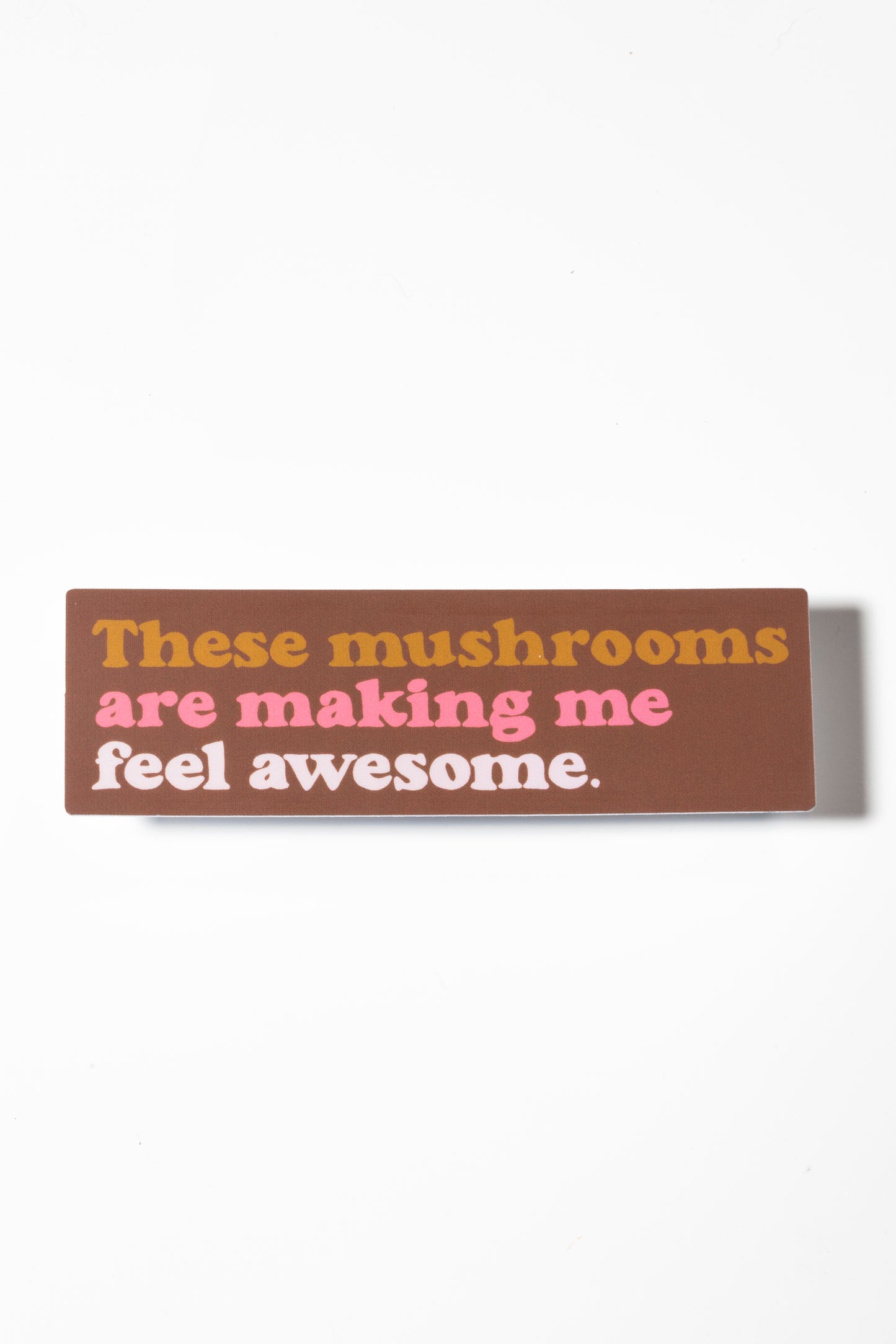 Brown sticker that reads "These mushrooms are making me feel awesome" in yellow and pink shot on a white background.