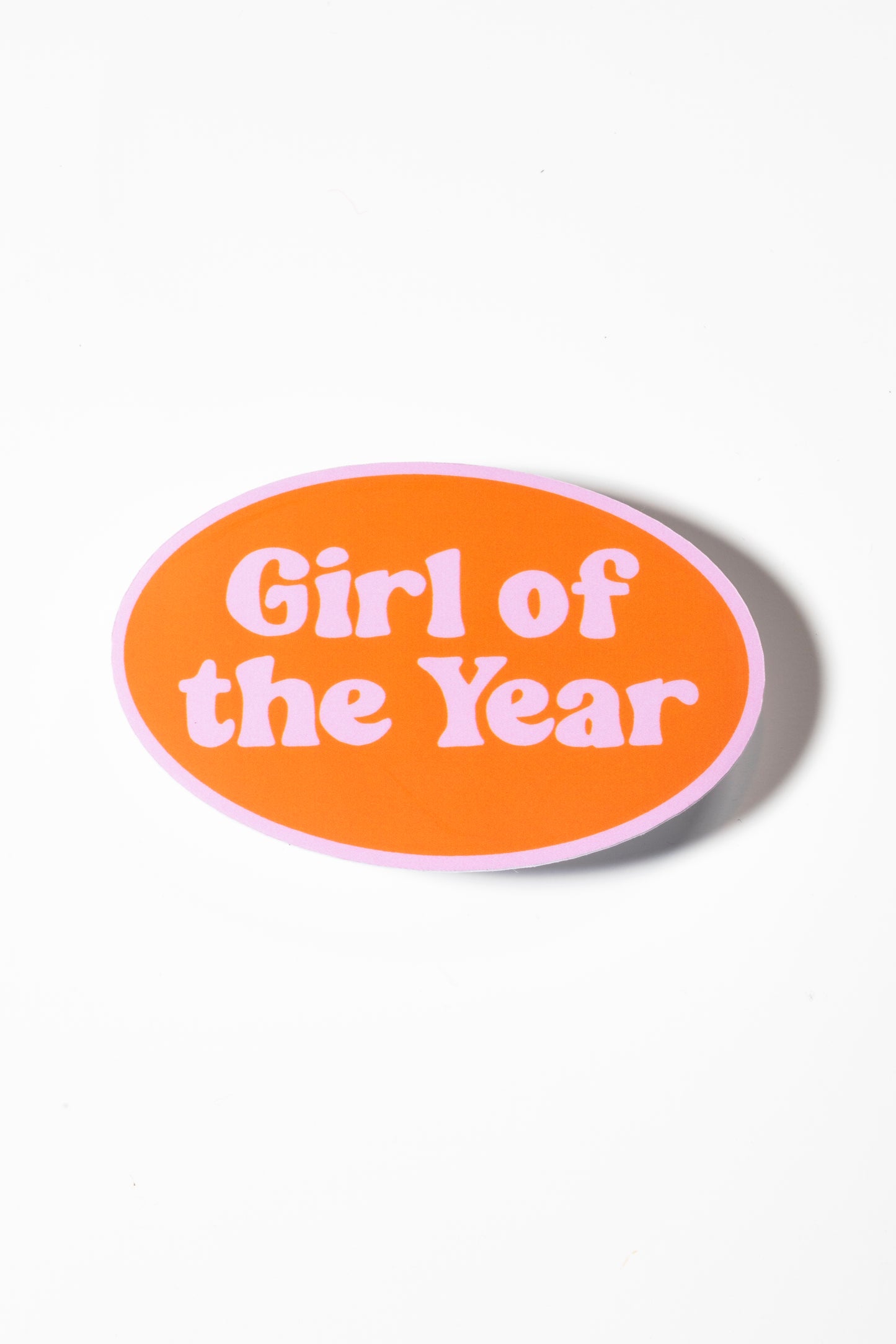 Sticker that says "Girl of the Year" in a pink, retro font on an orange oval shot on a white background.