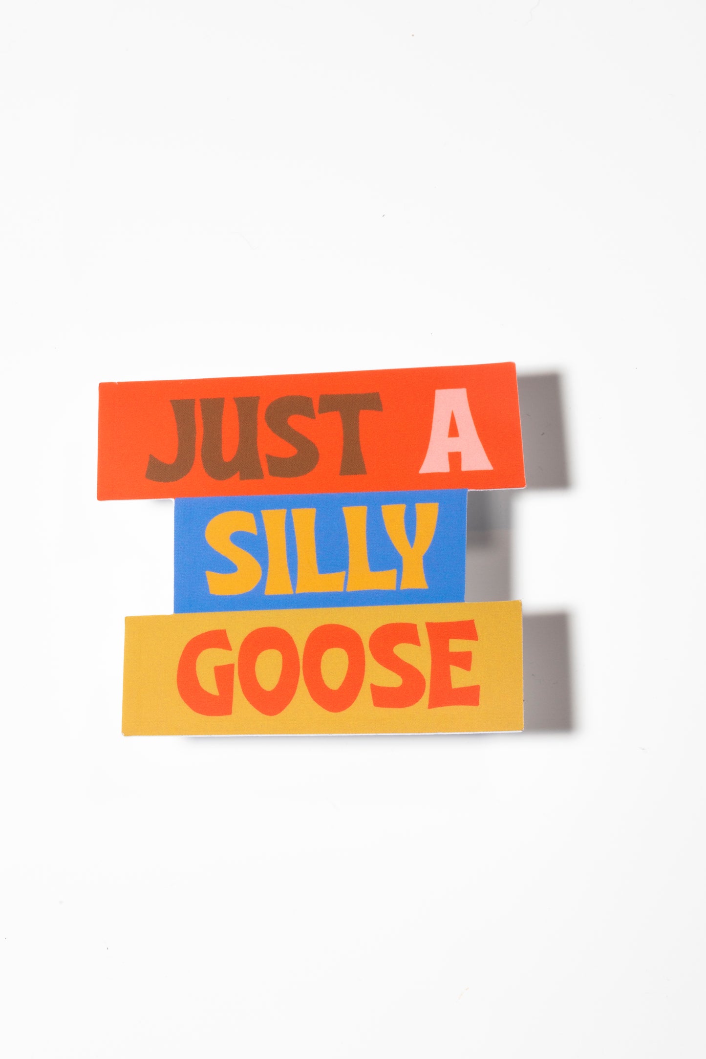 Fun sticker that reads "Just a Silly Goose" with a variety of colored backgrounds including red, yellow, and blue all photographed with a white background.