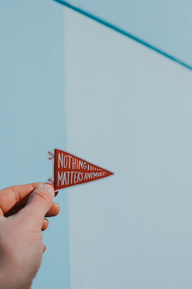 Pendant sticker that reds "nothing matters anymore" held by a hand against a blue background.