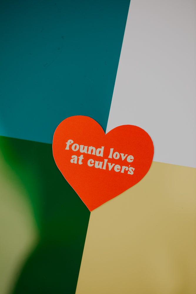 An orange heart-shaped sticker reading 'found love at culvers' placed on a geometric background divided into teal, white, forest green, and cream colored sections