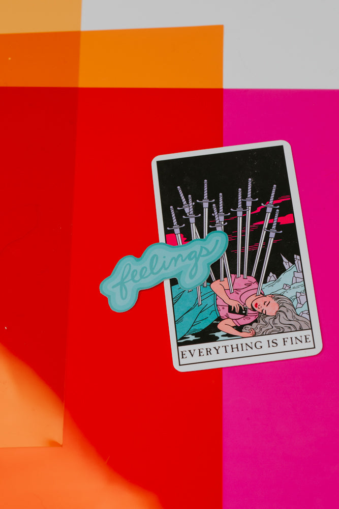 A turquoise 'feelings' sticker placed on top of a tarot-style card reading 'EVERYTHING IS FINE' showing multiple swords, against a vibrant background of orange, red, and pink"