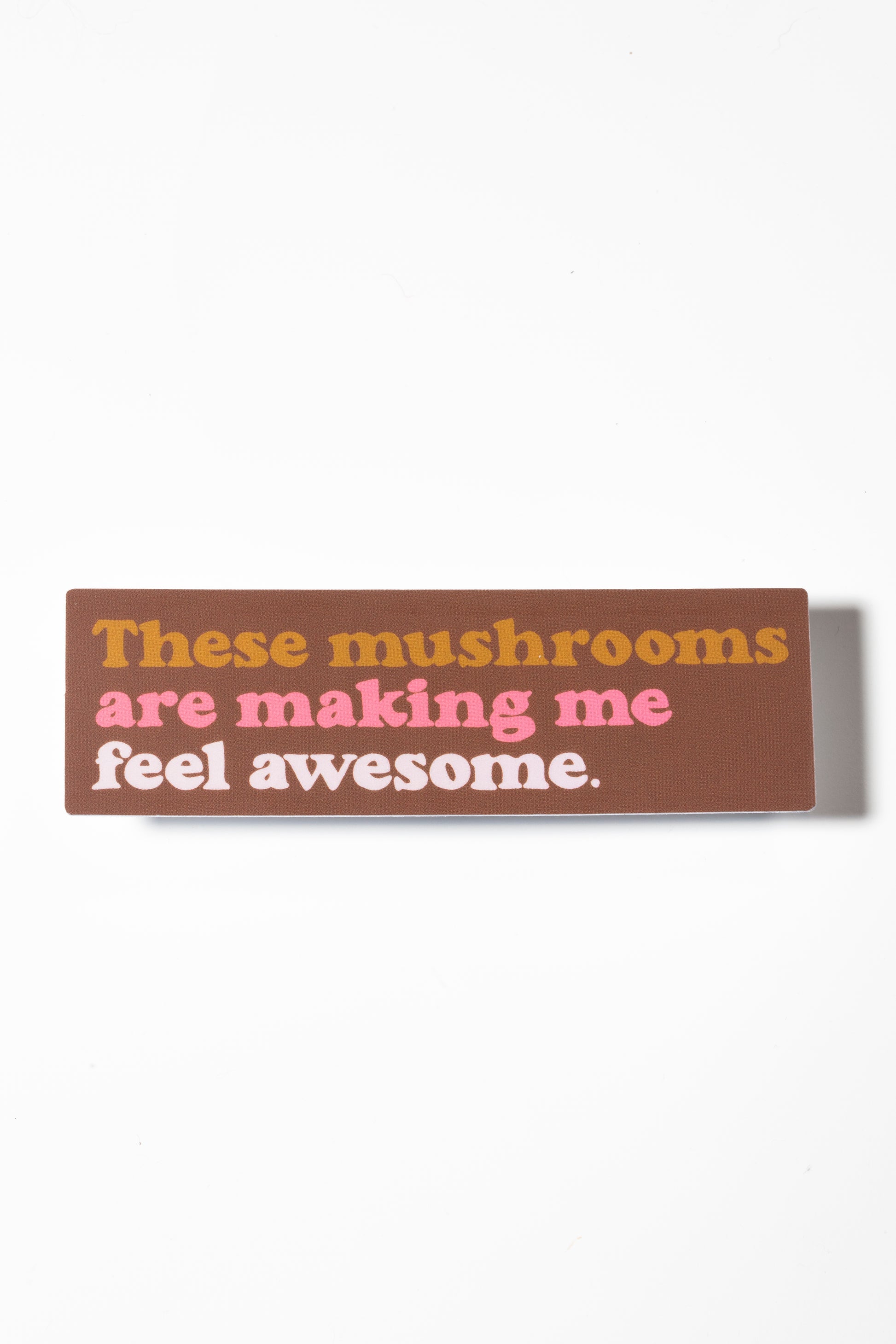 Brown sticker that reads "These mushrooms are making me feel awesome" in yellow and pink shot on a white background.