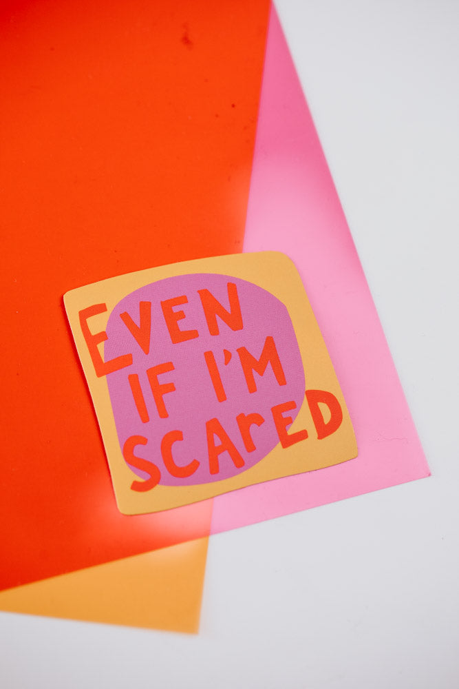 An image showing a close-up of a single square sticker with the text "Even if I'm scared" written in red letters on an orange background, placed against a pink and orange geometric background.